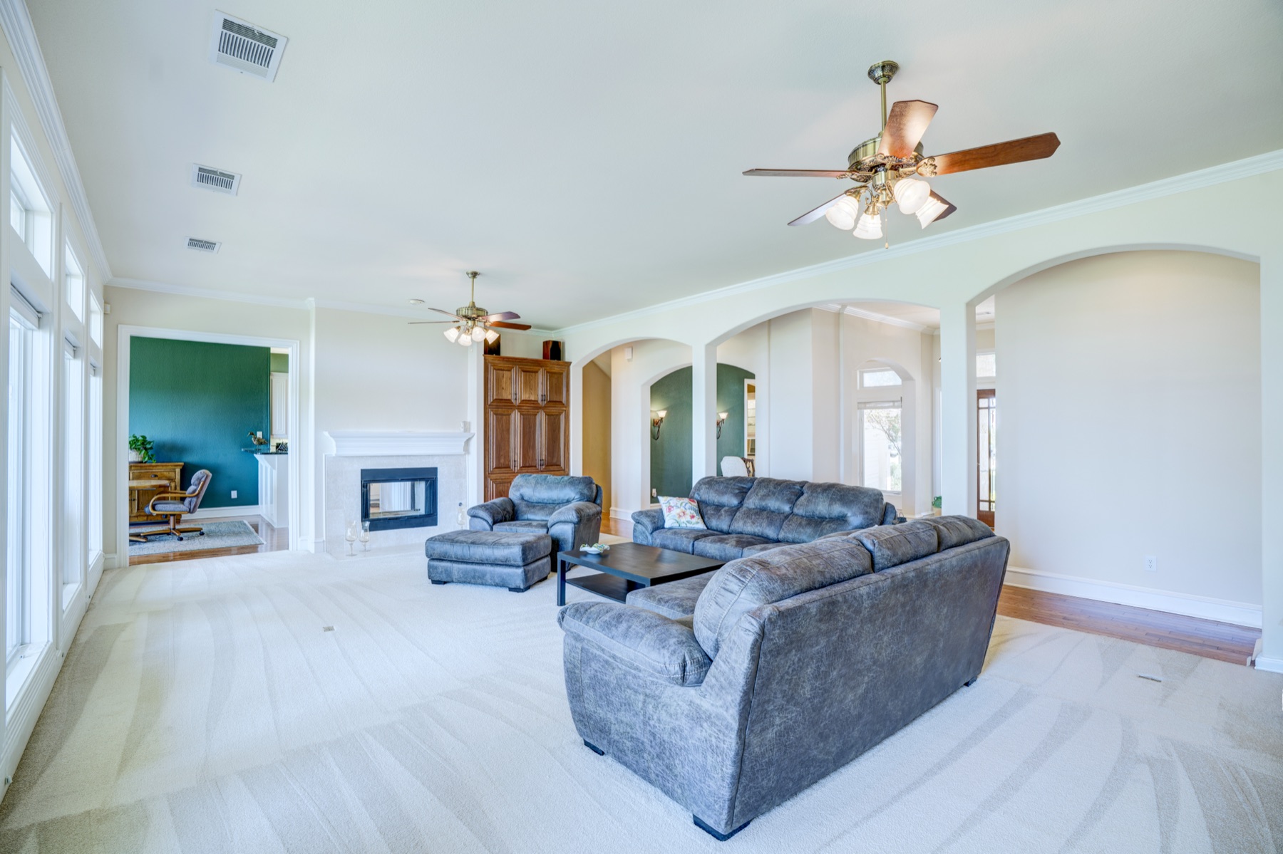 A second living area on the main floor: vaulted ceilings, arched openings to adjoining rooms, large windows on the left wall, two seating zones around a quiet stone fireplace.