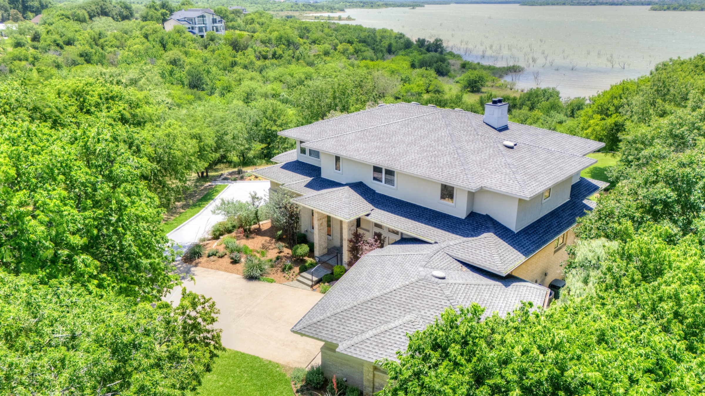 Aerial view of 1132 Mallard Pointe Drive: a three-level lakefront estate sitting on a wooded peninsula above Joe Pool Lake, with the lake bridge visible in the distance.